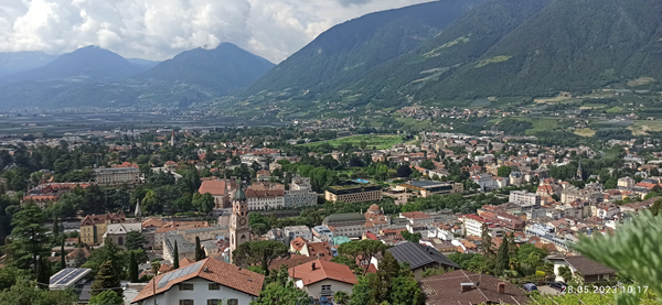 Erhöhter Blick auf die Stadt Meran in Südtirol. Man sieht die Altstadt sowie das Hinterland und die umgebenden Berge.